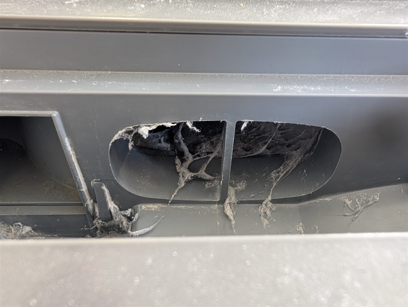 洗濯機裏側の排気口まわりに入った亀裂と漏れ出した埃